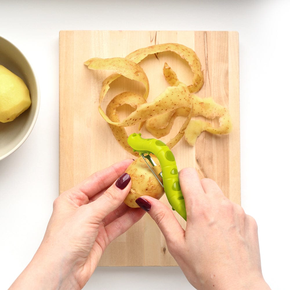 A fruit & vegetable peeler that looks like a green caterpillar. The peeler is show overhead peeling off potato skin